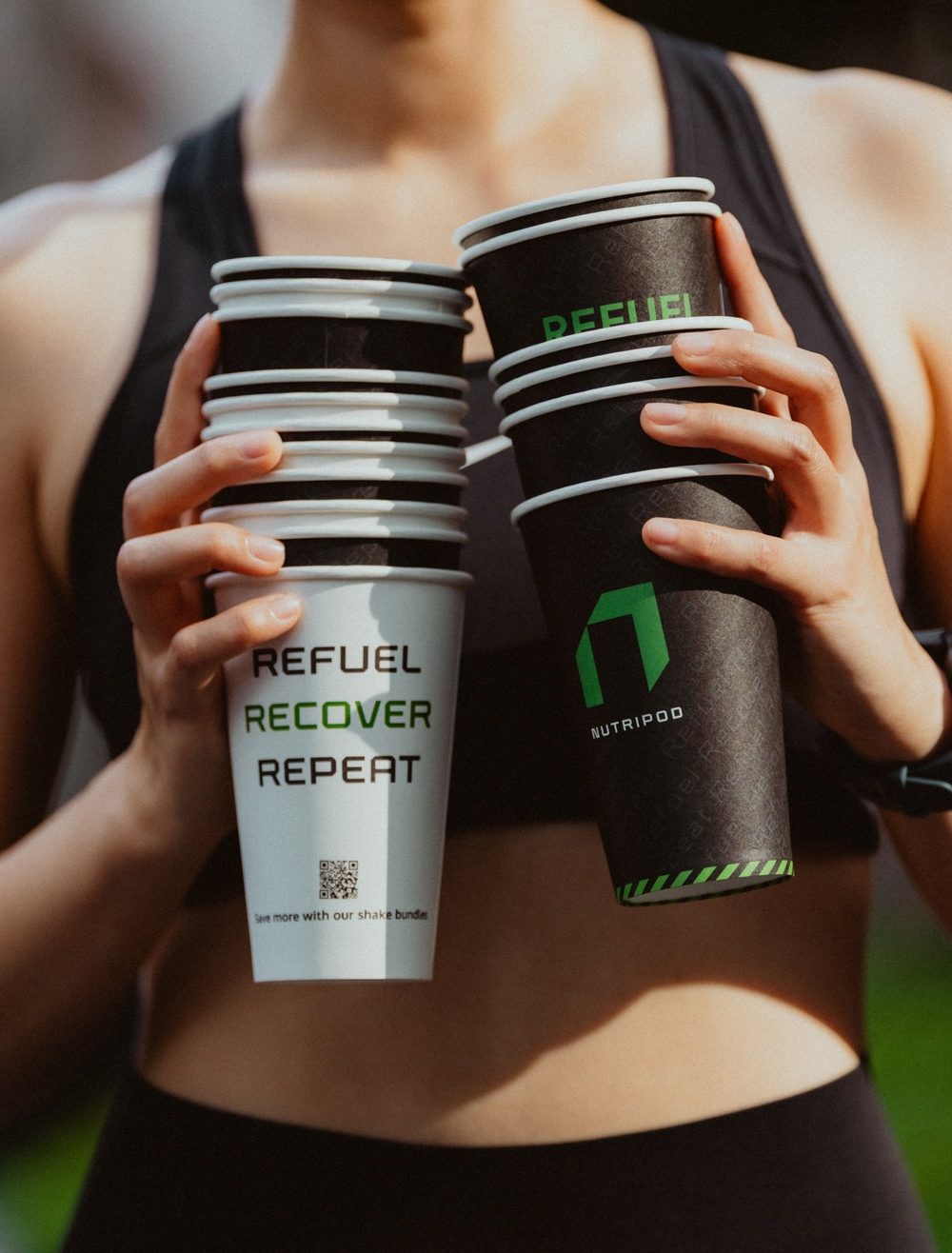 Athlete holding two stacks of NutriPod Refuel Recover Repeat shake cups